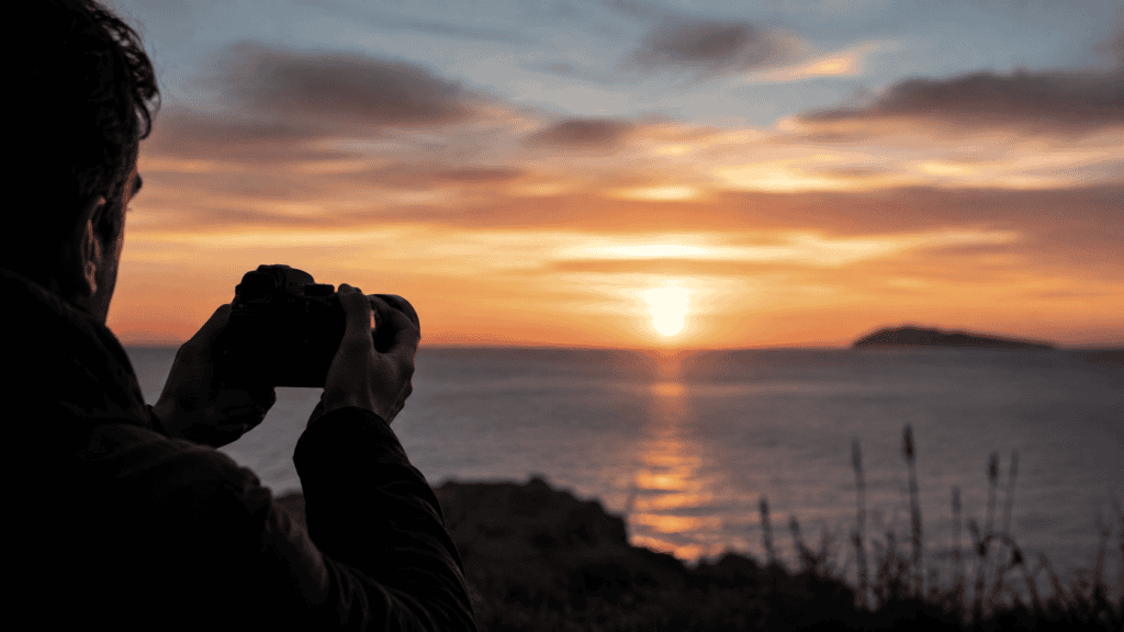 Mani che tengono una macchina fotografica abbassata davanti a un paesaggio di borgo italiano al tramonto